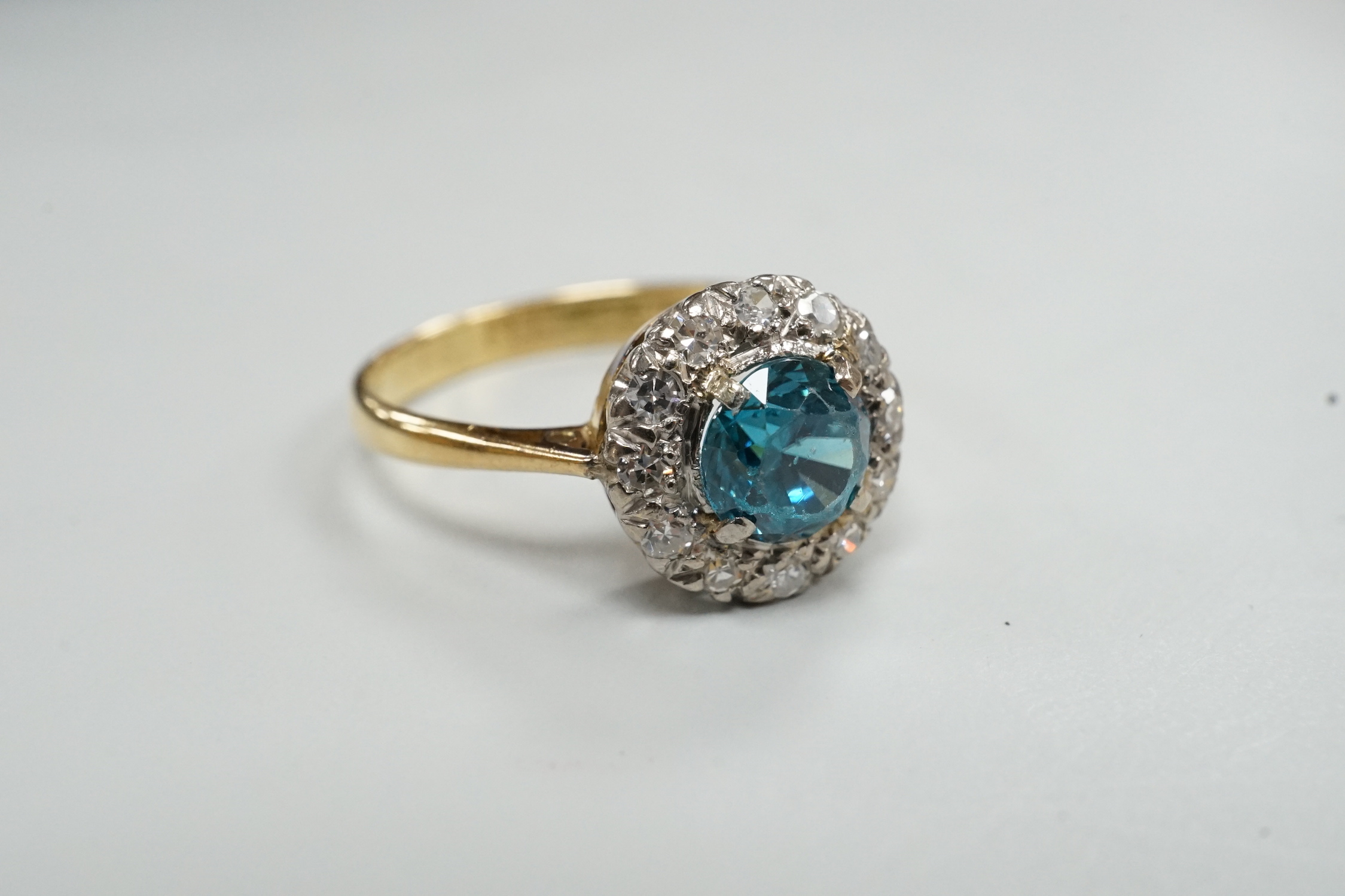 An 18ct & plat, blue zircon and illusion set diamond chip circular cluster ring, size M, gross weight 2.7 grams.